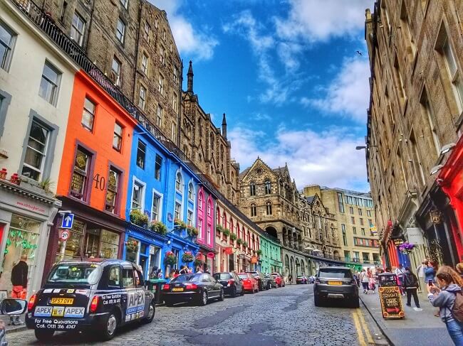 Victoria street which has old Georgian-style buildings, a few of them painted in bright colours, with cars parked on the sides and pedestrians walking on the pavements